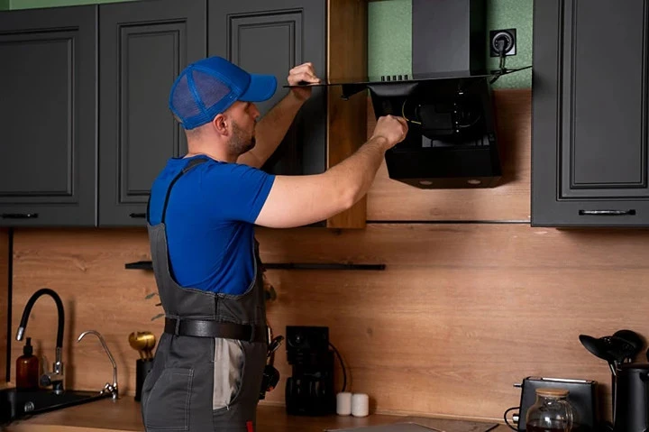 A handyman in uniform, installs or repairs a kitchen hood, replaces the filter in the hood.